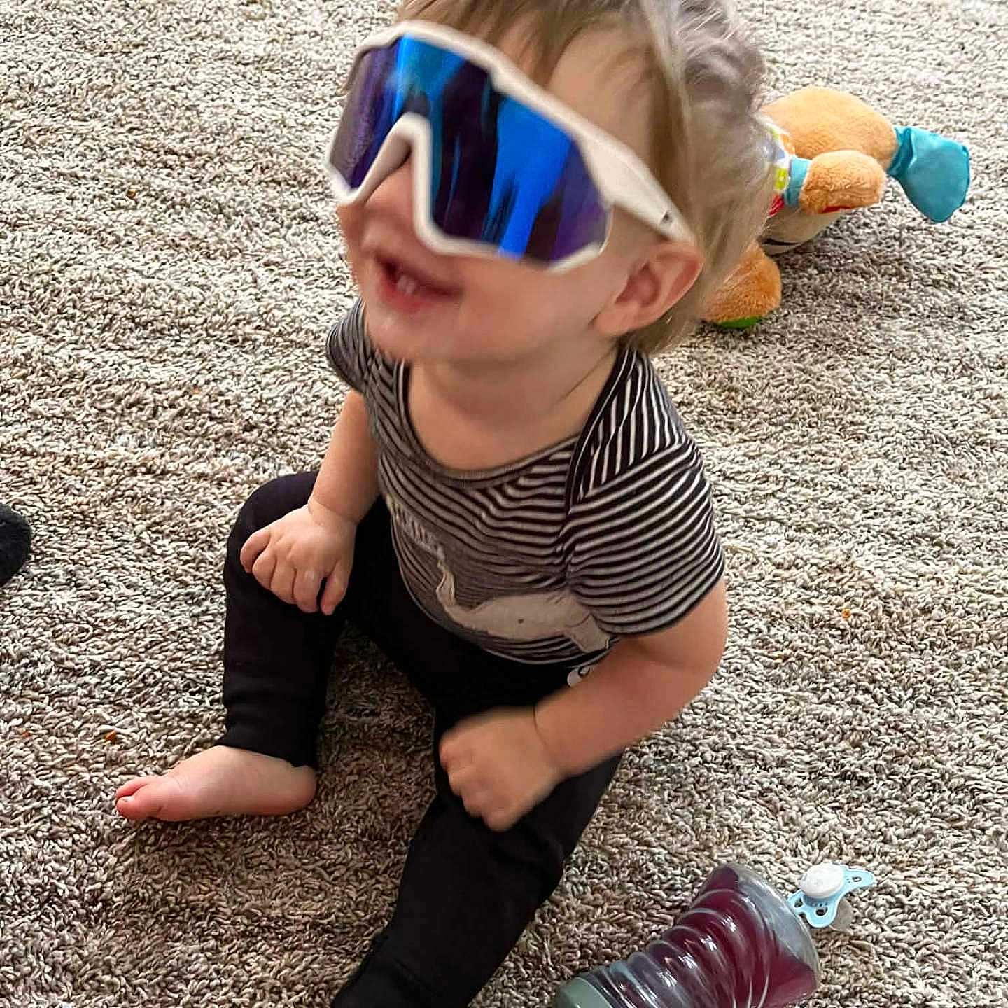 Drake joined the competition — help win amazing prizes! toddler, child, sunglasses, carpet, toy, stuffed_animal, sippy_cup, sitting, indoor, happy, smiling, clothing, striped_shirt, black_pants, barefoot, cute, playtime, home, fun, young_child