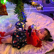 Hanny is registered to the contest to win money with this photo: baby, child, christmas_tree, ornament, holiday, festive, decorations, tree_skirt, red_clothing, floor, toy, unicorn, lights, reflection, indoor, curly_hair, socks, plush, celebration, holiday_season