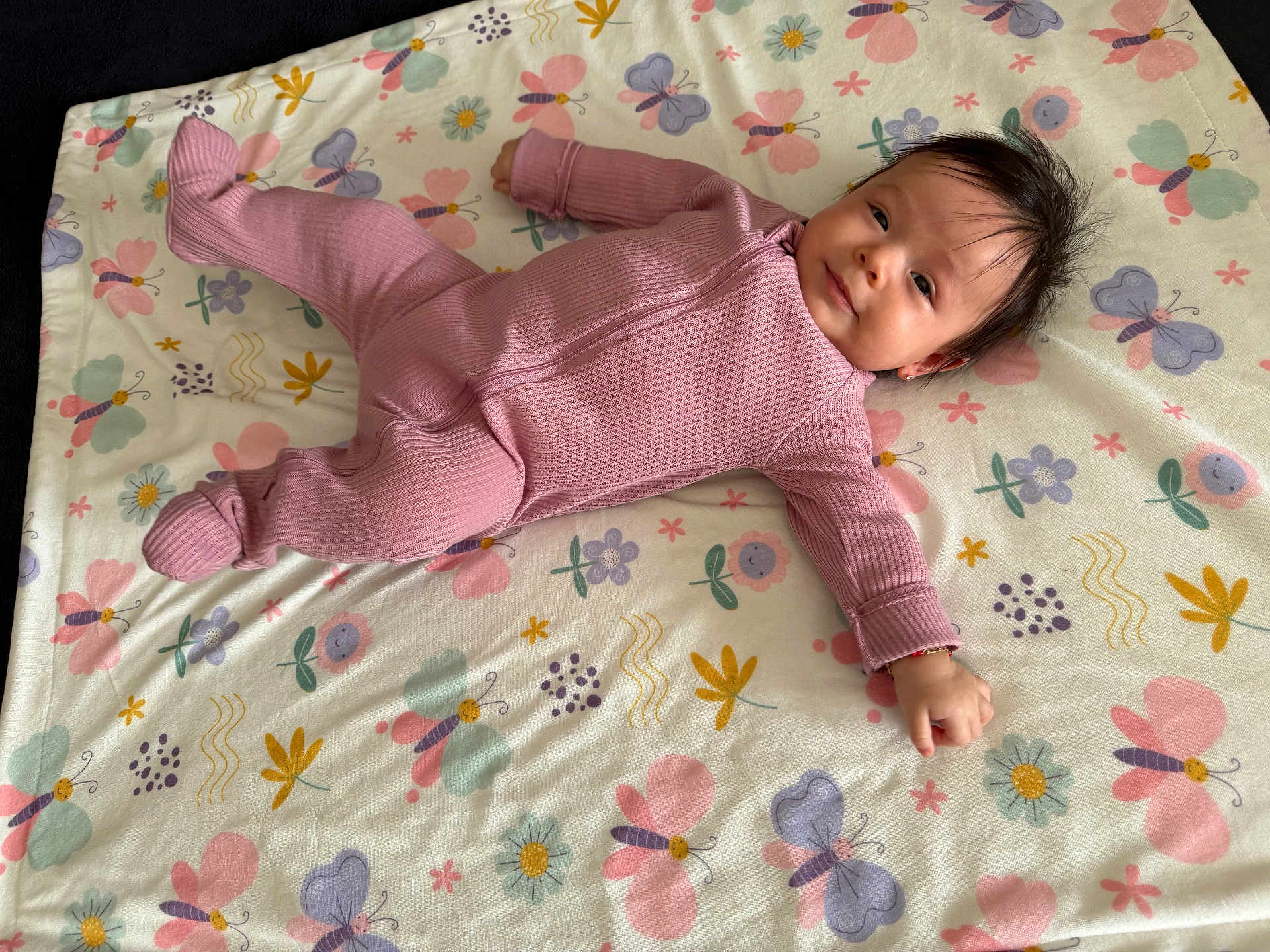 Hanny is registered to the contest to win money with this photo: baby, infant, pink_onesie, blanket, butterfly_pattern, flower_pattern, smiling, lying_down, cute, child, toddler, indoors, soft_texture, cozy, portrait, young_child, head, face, happy, casual