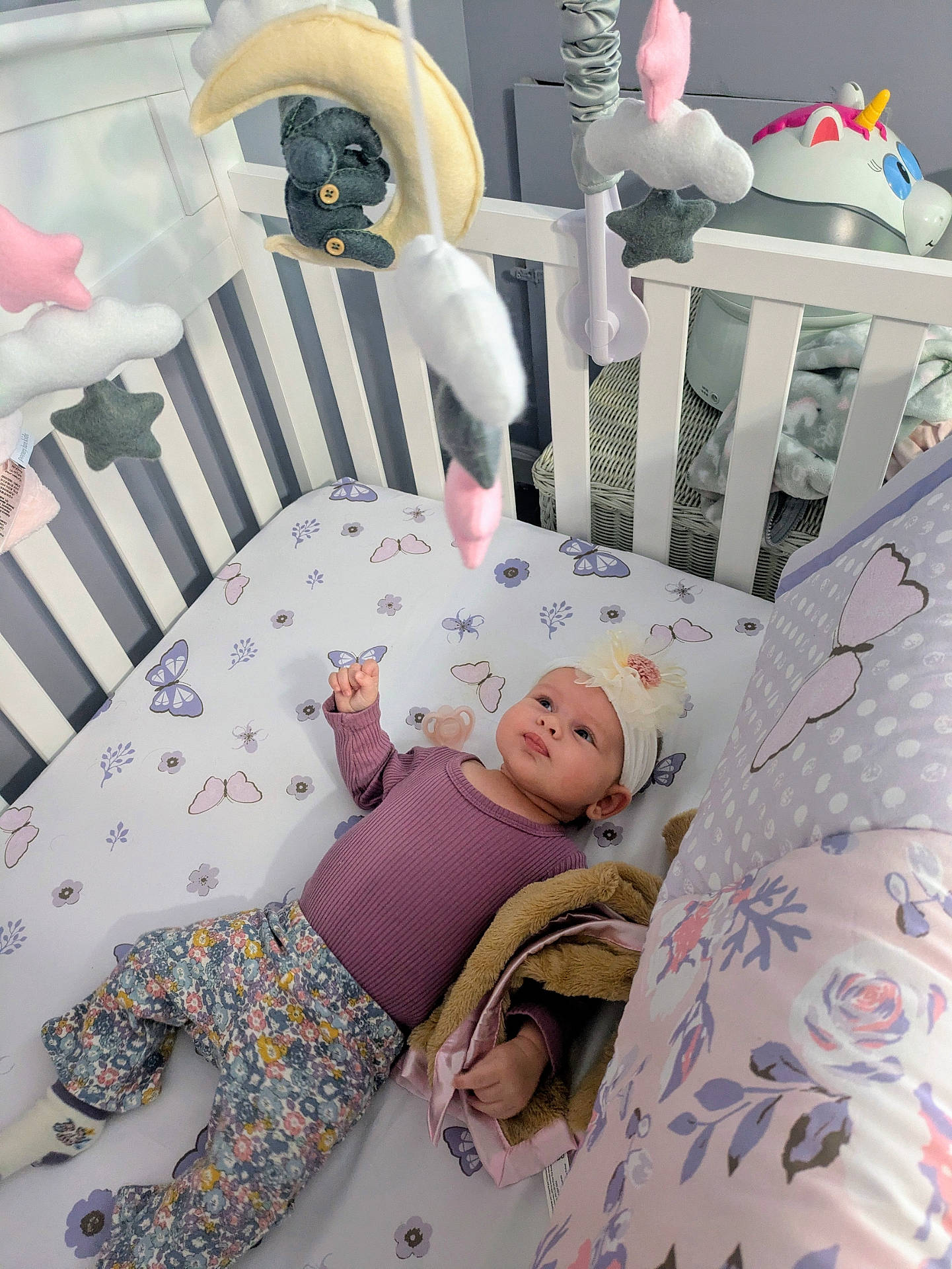 Brea is registered to the contest to win money with this photo: baby, blanket, butterfly_pattern, child, clothing, crib, cute, decor, flower_pattern, headband, indoor, infant, mobile, nursery, person, pillow, purple, sleeping_area, soft_toys, stuffed_toy