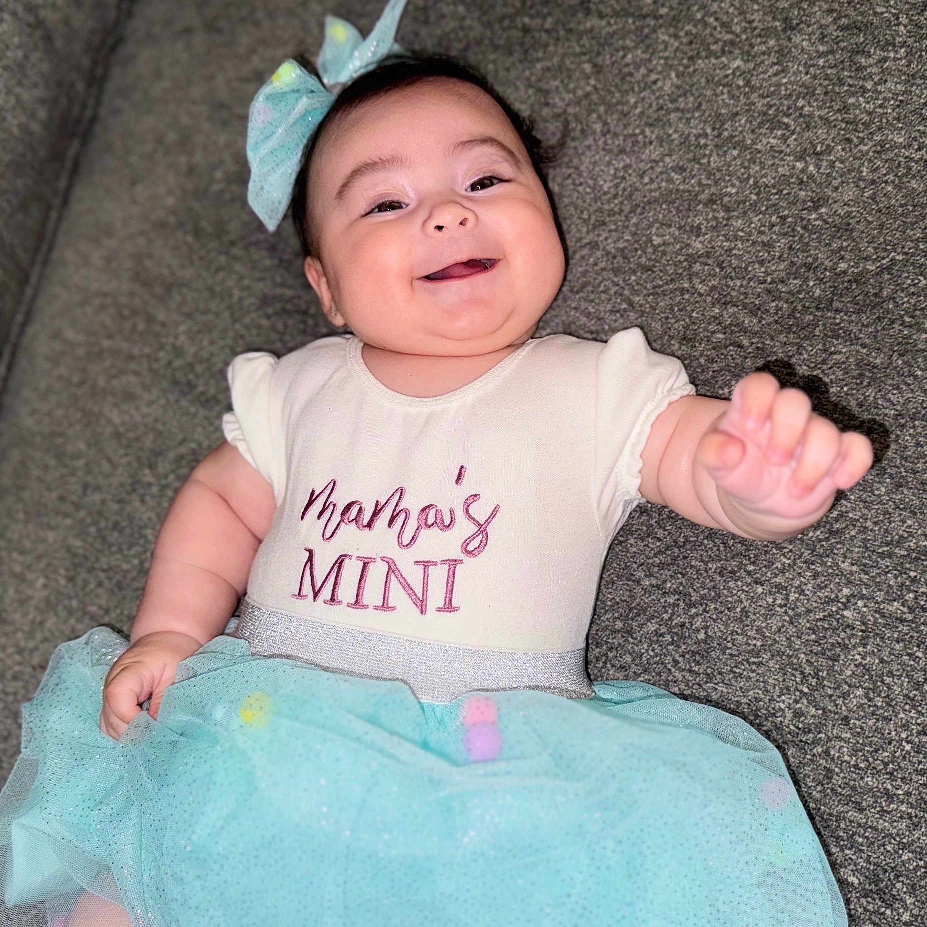 Ebony is registered to the contest to win money with this photo: baby, bow, celebration, child, clothing, couch, cute, cute_expression, dress, fabric, fun, happy, indoor, infant, person, portrait, sitting, smiling, soft, tutu