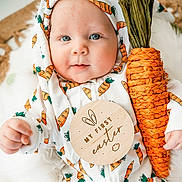 Charlie is registered to the contest to win money with this photo: baby, infant, child, blue_eyes, carrot_pattern, carrot_prop, easter_plaque, wooden_sign, hood, onesie, cute, portrait, closeup, soft_blanket, hand, smile, holiday, props, fabric_pattern, woven_decor