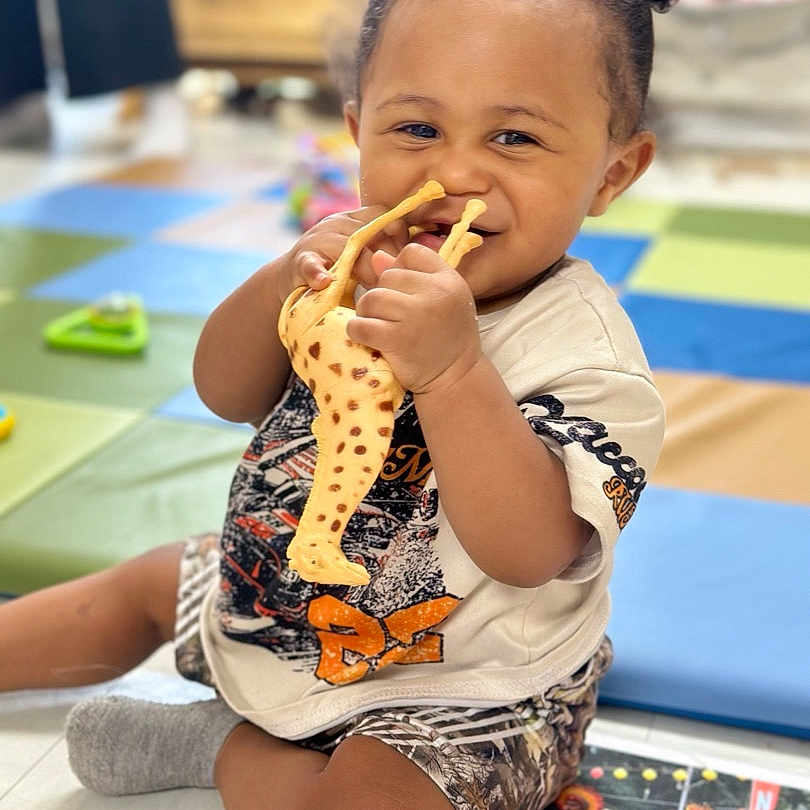 Kaizen joined the competition — help win amazing prizes! toddler, child, toy, giraffe, smiling, indoor, play_mat, cross_legged, happy, cute, hair_buns, shorts, tshirt, floor, colorful, playtime, person, baby, young_child, joyful