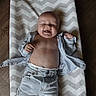 baby, smiling, shirt, jeans, floor, mat, chevron_pattern, happy, child, infant, clothing, casual, bare_chest, indoor, cute, person, portrait, playful, relaxed, young