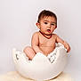 Maë participe au concours pour gagner de l'argent avec cette photo : baby, child, necklace, eggshell, white_background, fur_rug, studio_photo, cute, naked_torso, indoors, portrait, sitting, curious, young_child, soft_lighting, props, isolated, baby_boy, expression, minimalist