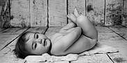 Maë a rejoint le concours — aidez-le/la à gagner de superbes lots ! baby, infant, naked, lying_down, fur_rug, wooden_floor, black_and_white, portrait, expression, curious, soft_light, texture, background, skin, head, face, newborn, child, resting, peaceful
