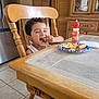 Nicholas joined the competition — help win amazing prizes! child, boy, smiling, eating, fries, corn_dog, plate, ketchup, drink_bottle, wooden_chair, kitchen, table, tile_floor, cabinet, curly_hair, happy, indoor, meal, person, home