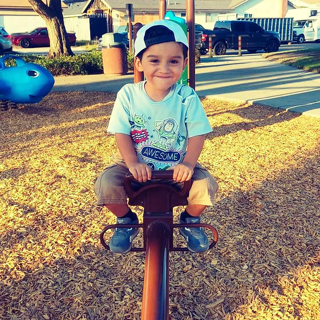 Nicholas is registered to the contest to win money with this photo: boy, cap, car, child, daylight, footwear, happy, outdoor, park, person, play_equipment, playground, recreation, residential, seesaw, smile, toy_story, tree, tshirt, wood_chips
