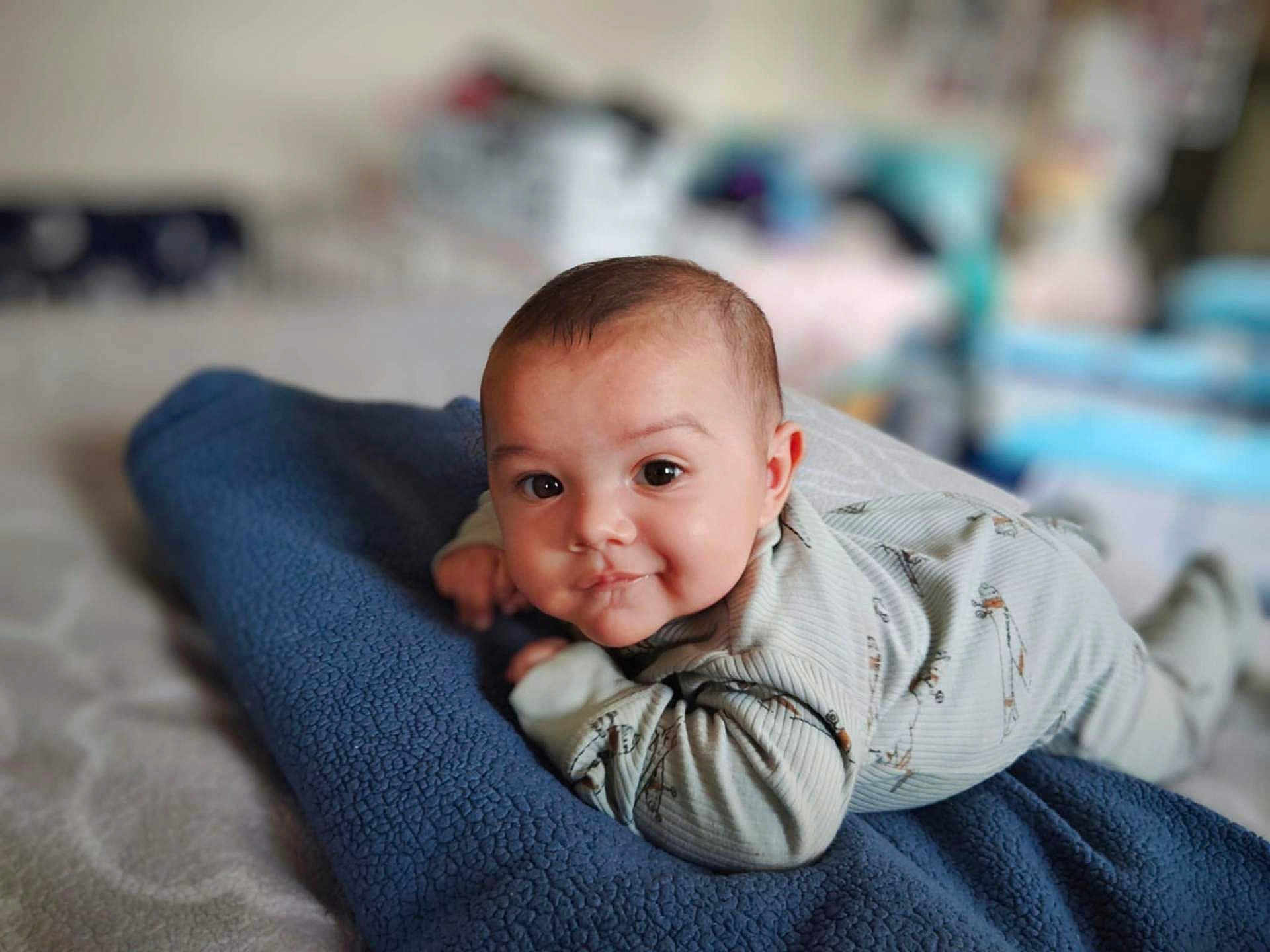 Eli joined the competition — help win amazing prizes! baby, infant, blanket, bed, clothing, face, person, portrait, smile, cute, young, lying_down, indoors, soft_focus, cozy, child, sleepwear, expression, head, skin