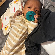 Mada is registered to the contest to win money with this photo: baby, pacifier, striped_onesie, infant, sleepy, baby_wipes, black_cloth, bed, blanket, toddler, young_child, indoor, face, hand, clothing, soft_toys, comfort, resting, cute, child