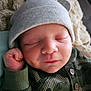 baby, newborn, sleeping, hat, green_clothing, blanket, closeup, infant, peaceful, soft_texture, cute, portrait, resting, cozy, child, face, hand, buttoned_shirt, indoors, warm