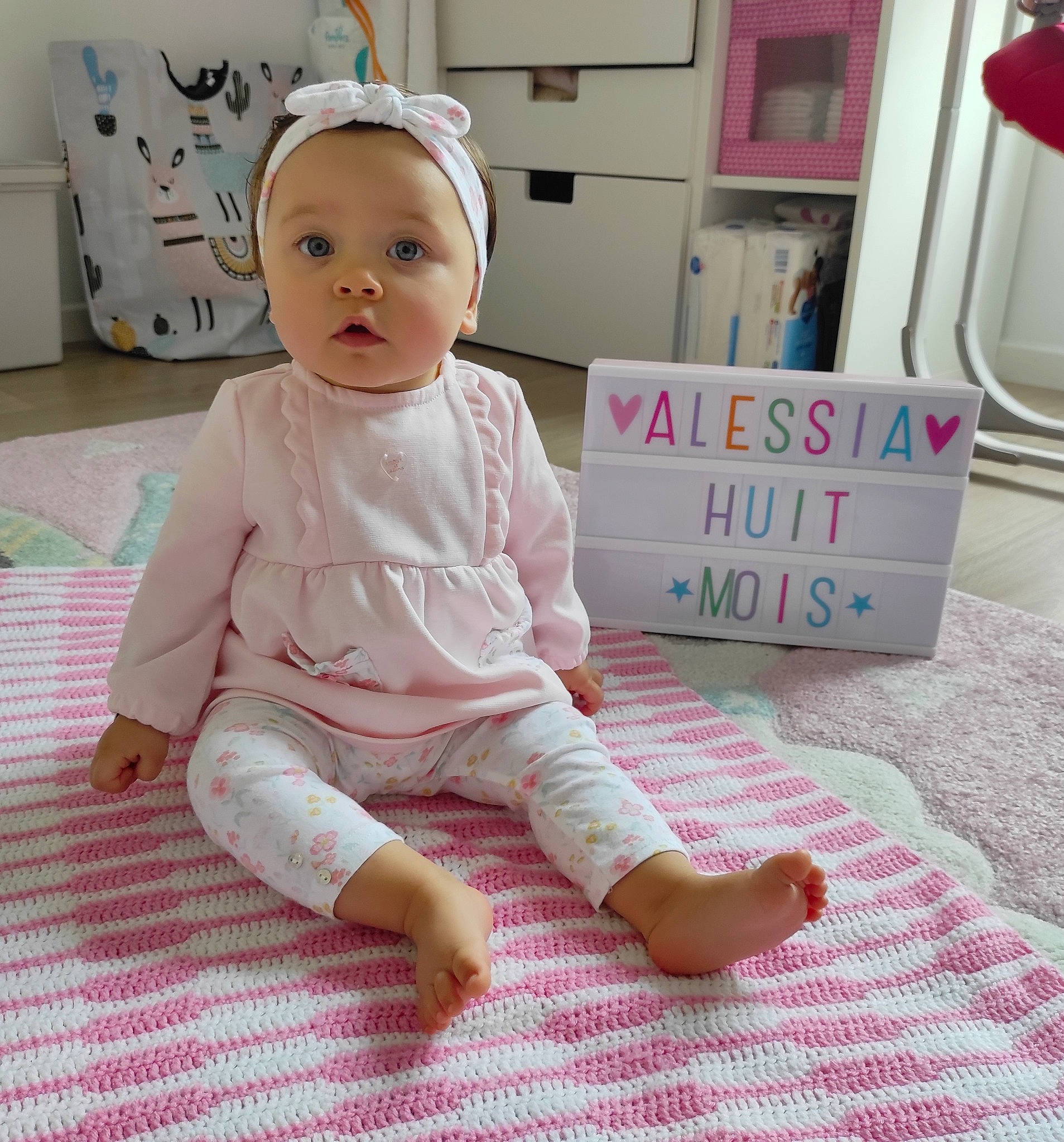 Alessia a rejoint le concours — aidez-le/la à gagner de superbes lots ! baby, baby_products, baby_safety, baby_toddler_clothing, barefoot, cheek, child, comfort, floor, flooring, foot, happy, linens, magenta, person, pink, sitting, skin, sleeve, surprise