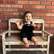 Liv is registered to the contest to win money with this photo: toddler, child, bench, wooden_bench, brick_wall, smiling, happy, barefoot, curly_hair, overalls, outdoor, floor, rustic, portrait, cute, person, sitting, playful, casual, daylight