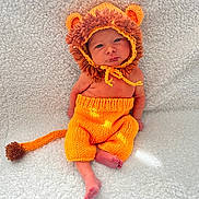 Oakley joined the competition — help win amazing prizes! baby, infant, knitted_clothing, lion_costume, orange, brown, hat, tail, blanket, soft_texture, cute, child, portrait, sitting, indoors, newborn, warm, cozy, face, feet