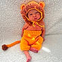 baby, infant, knitted_clothing, lion_costume, orange, brown, hat, tail, blanket, soft_texture, cute, child, portrait, sitting, indoors, newborn, warm, cozy, face, feet