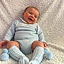 Oakley is registered to the contest to win money with this photo: baby, smiling, sitting, blue_clothing, knitwear, pom_poms, socks, blanket, cozy, happy, cute, infant, child, portrait, indoor, texture, soft, warm, person, face