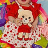 baby, child, smiling, red_dress, heart_pattern, unicorn, rainbow, play_mat, colorful, cute, happy, infant, toy, footwear, bracelet, background, pink, purple, white, accessories
