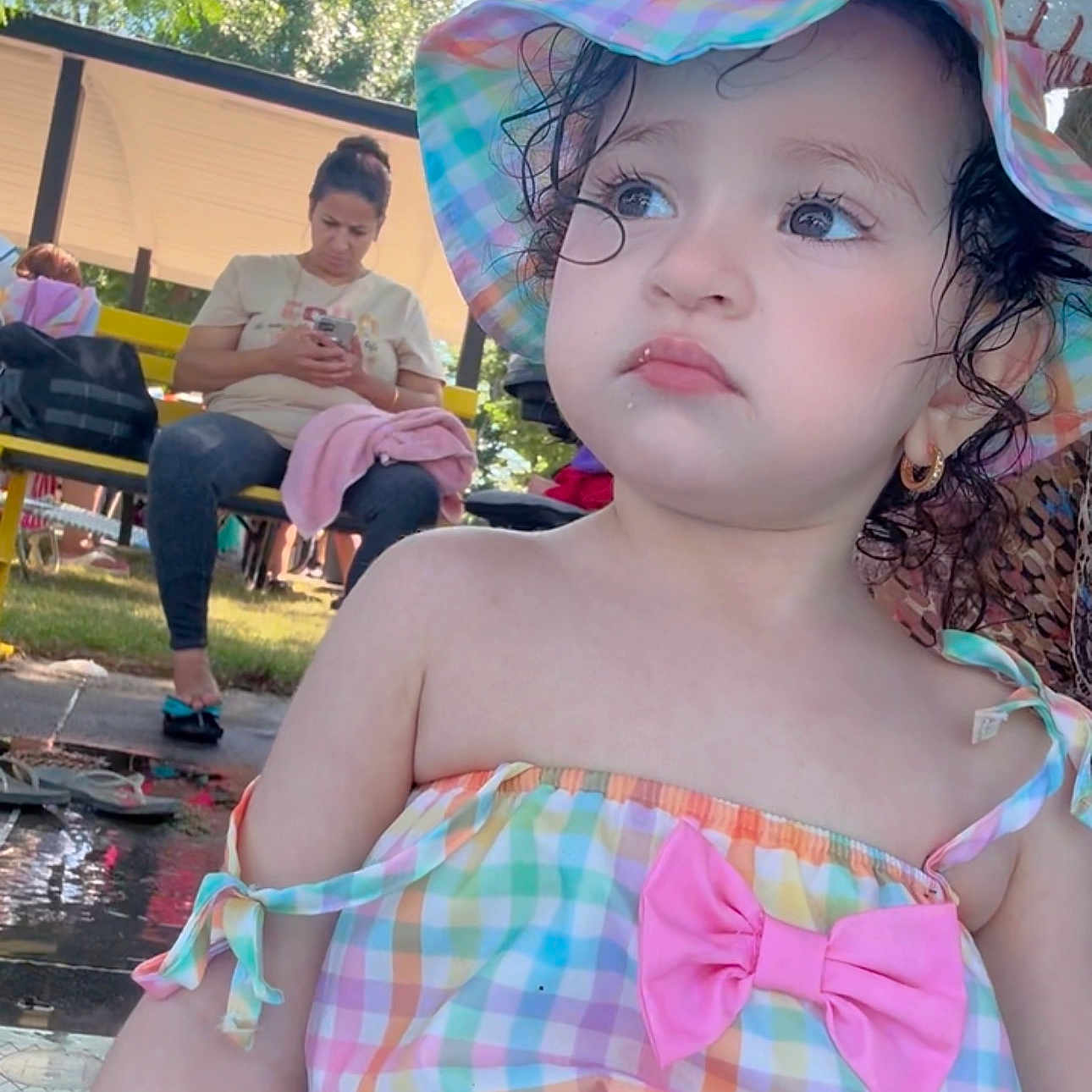 Melissia joined the competition — help win amazing prizes! toddler, child, outdoor, hat, colorful_clothing, pink_bow, curly_hair, person, woman, bench, phone, sunlight, trees, summer, portrait, casual, expression, daytime, nature, recreation