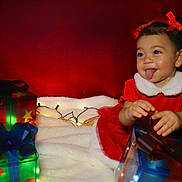 Nyla joined the competition — help win amazing prizes! toddler, child, girl, red_dress, holiday, christmas, presents, gift_boxes, lights, smile, tongue_out, cute, festive, celebration, happy, indoors, portrait, holiday_decor, holiday_lights, soft_blanket