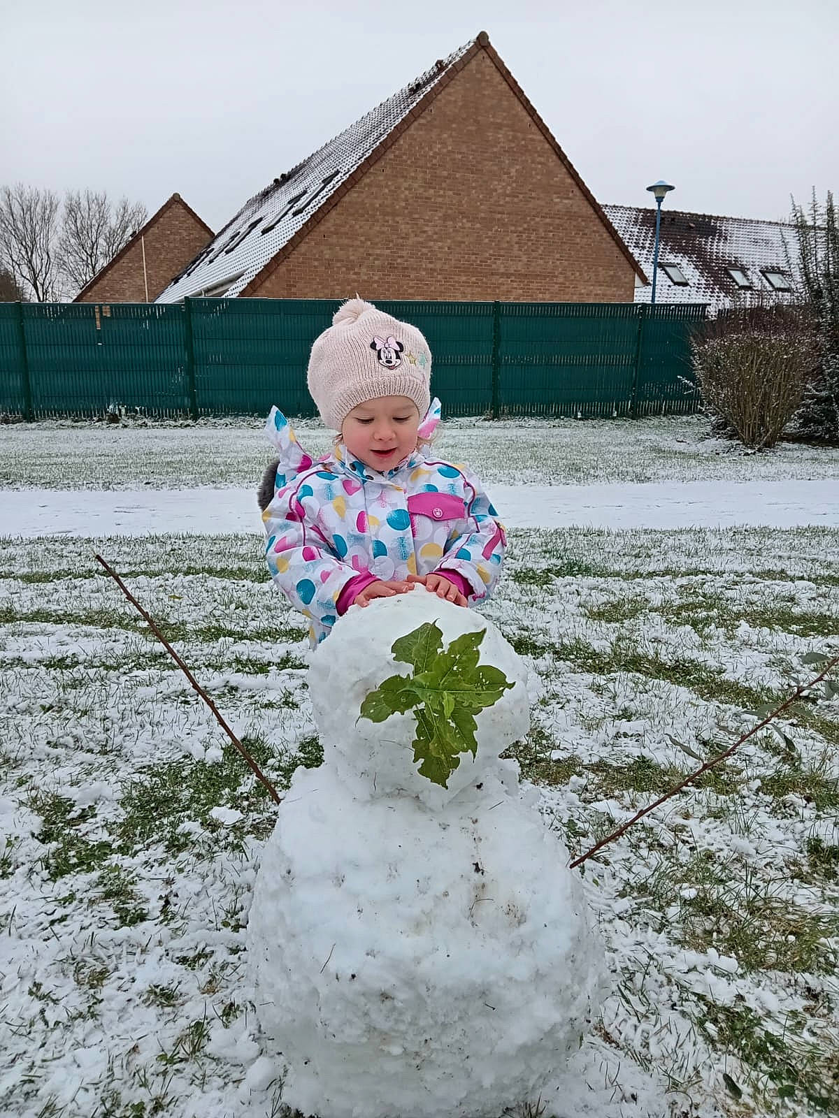 Mïa participe au concours pour gagner de l'argent avec cette photo : baby_toddler_clothing, child, face, freezing, fun, grass, happy, head, headwear, house, outerwear, people_in_nature, person, plant, recreation, sky, slope, snow, snowman, toddler