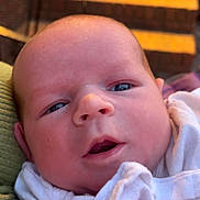 Liam is registered to the contest to win money with this photo: baby, newborn, infant, face, close_up, blanket, white_clothing, skin, head, eyes, mouth, brick, stairs, background, indoors, soft_light, person, portrait, child, cute