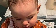 Violet is registered to the contest to win money with this photo: baby, child, infant, toddler, hair_ties, purple, onesie, orange, floral_pattern, bed, pillow, headboard, face, skin, arms, indoor, focused, cute, sitting, plastic_container