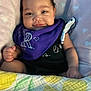 Milanie joined the competition — help win amazing prizes! baby, infant, smile, blanket, purple_bib, black_clothing, heart_pattern, cute, indoors, soft_texture, child, person, skin, face, happy, sitting, cozy, young, portrait, closeup