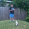 Pearl Baehr is registered to the contest to win money with this photo: boy, puppy, dog, leash, grass, fence, backyard, tree, bush, child, casual_clothing, outdoor, summer, pet, playing, young, nature, animal, curious, standing