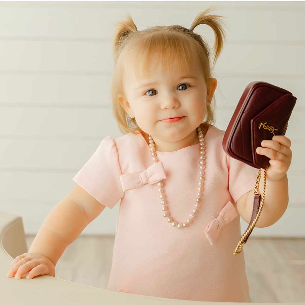 Emilia Marie joined the competition — help win amazing prizes! accessory, bow, child, cute, fashion, girl, handbag, happy, indoor, light_background, luxury, pearl_necklace, person, pigtails, pink_dress, portrait, smile, standing, toddler, young_child