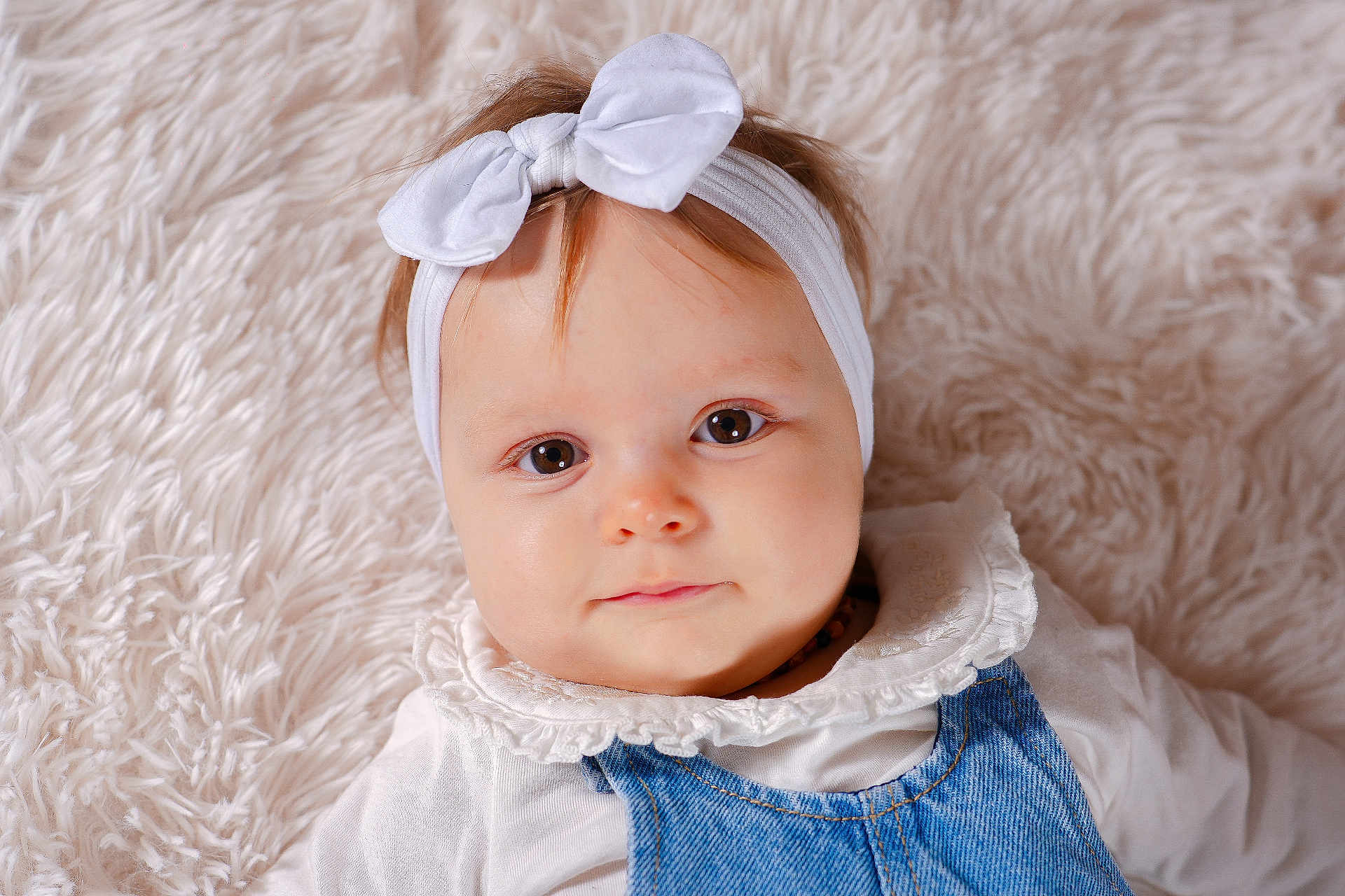 Agathe participe au concours pour gagner de l'argent avec cette photo : baby, child, headband, bow, denim, overalls, white_shirt, frilly_collar, fluffy_blanket, close_up, portrait, cute, infant, face, eyes, skin, hair, lying_down, indoors, soft_texture
