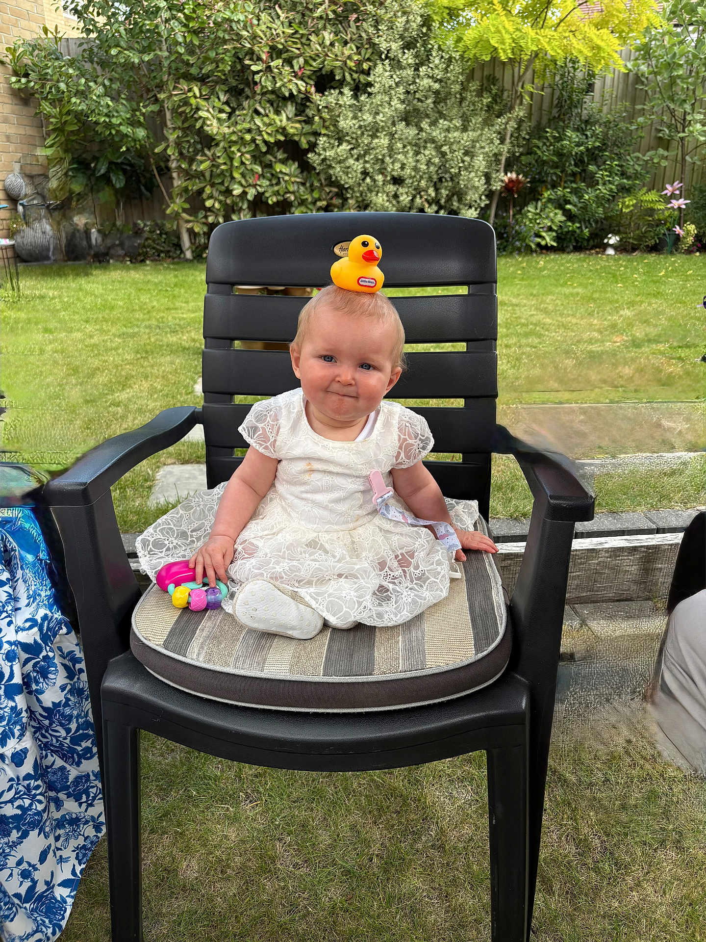 Daisy-Mae joined the competition — help win amazing prizes! baby, child, smile, white_dress, lace, rubber_duck, toy, chair, cushion, outdoor, garden, greenery, grass, plastic_chair, happy, person, cute, playful, head_accessory, infant
