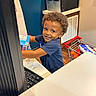 blue_shirt, blue_wall, cash_register, child, counter, curly_hair, fun, groceries, happy, indoor, keyboard, kid, person, play, pretend, retail, sign, smiling, store, toy_shopping_cart