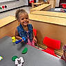 Arabella joined the competition — help win amazing prizes! child, smiling, denim_vest, playdough, playdough_tools, classroom, table, red_chair, curly_hair, educational, preschool, learning, happy, indoor, toy, kid, play, person, furniture, school