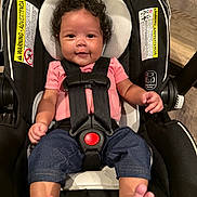 Avery joined the competition — help win amazing prizes! baby, child, car_seat, curly_hair, smiling, pink_shirt, blue_pants, feet, infant, seatbelt, portrait, indoors, cute, safety_harness, person, happy, closeup, young_child, head_support, foot