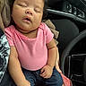 baby, sleeping, pink_shirt, blue_pants, blanket, car_interior, steering_wheel, hand, child, person, seat, clothing, curly_hair, peaceful, cute, portrait, indoor, infant, relaxed, toddler