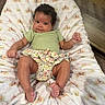 baby, infant, curly_hair, green_shirt, floral_diaper_cover, blanket, princess_theme, crown_pattern, soft_fabric, wood_floor, wood_furniture, indoors, cute, smiling, relaxed, person, child, small_hands, small_feet, portrait