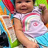 baby, curly_hair, smiling, onesie, rainbow, baby_seat, colorful, green_frog, patterned, infant, cute, happy, child, indoor, clothing, small_fist, bright_colors, portrait, young_child, seat