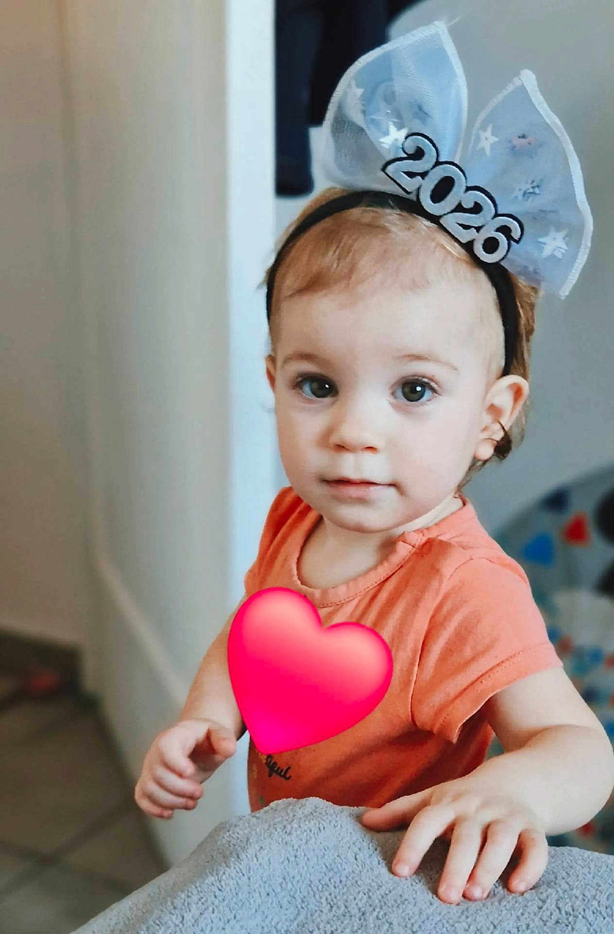Alexandra a rejoint le concours — aidez-le/la à gagner de superbes lots ! toddler, child, headband, 2026, orange_shirt, hand, face, eyes, indoor, soft_texture, curious, person, young_child, baby, portrait, cute, light, expression, skin, hair