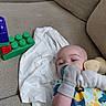 baby, infant, child, face, smiling, pacifier, plush_toy, blanket, couch, indoors, portrait, sitting, lying_down, colorful_clothing, building_blocks, toy, home, cozy, daylight, happy