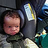 baby, infant, child, car_seat, car, vehicle, harness, seatbelt, curly_hair, serious_expression, face, portrait, sitting, blanket, clothing, indoor, transportation, safety_label, automotive, photography