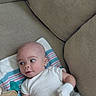 baby, infant, child, portrait, face, eyes, curious, lying_down, white_onesie, mittens, blanket, striped_blanket, pacifier, plush_toy, couch, cushions, indoor, home, soft_furnishings, photography