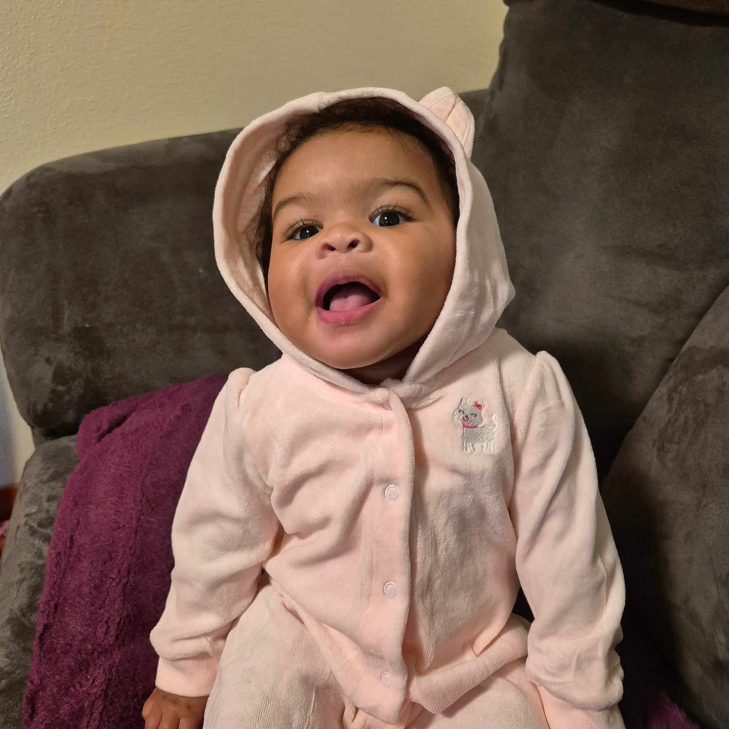 Malayah is registered to the contest to win money with this photo: baby, blanket, child, clothing, couch, cozy, cute, furniture, happy, hood, indoor, infant, person, pink_onesie, portrait, sitting, smiling, soft, warm, young_child