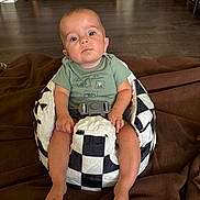 Gilberto joined the competition — help win amazing prizes! baby, child, infant, sitting, portrait, face, looking_at_camera, calm, indoors, blanket, cushion, baby_seat, safety_harness, green_shirt, bare_feet, hardwood_floor, living_room, furniture, home, photography