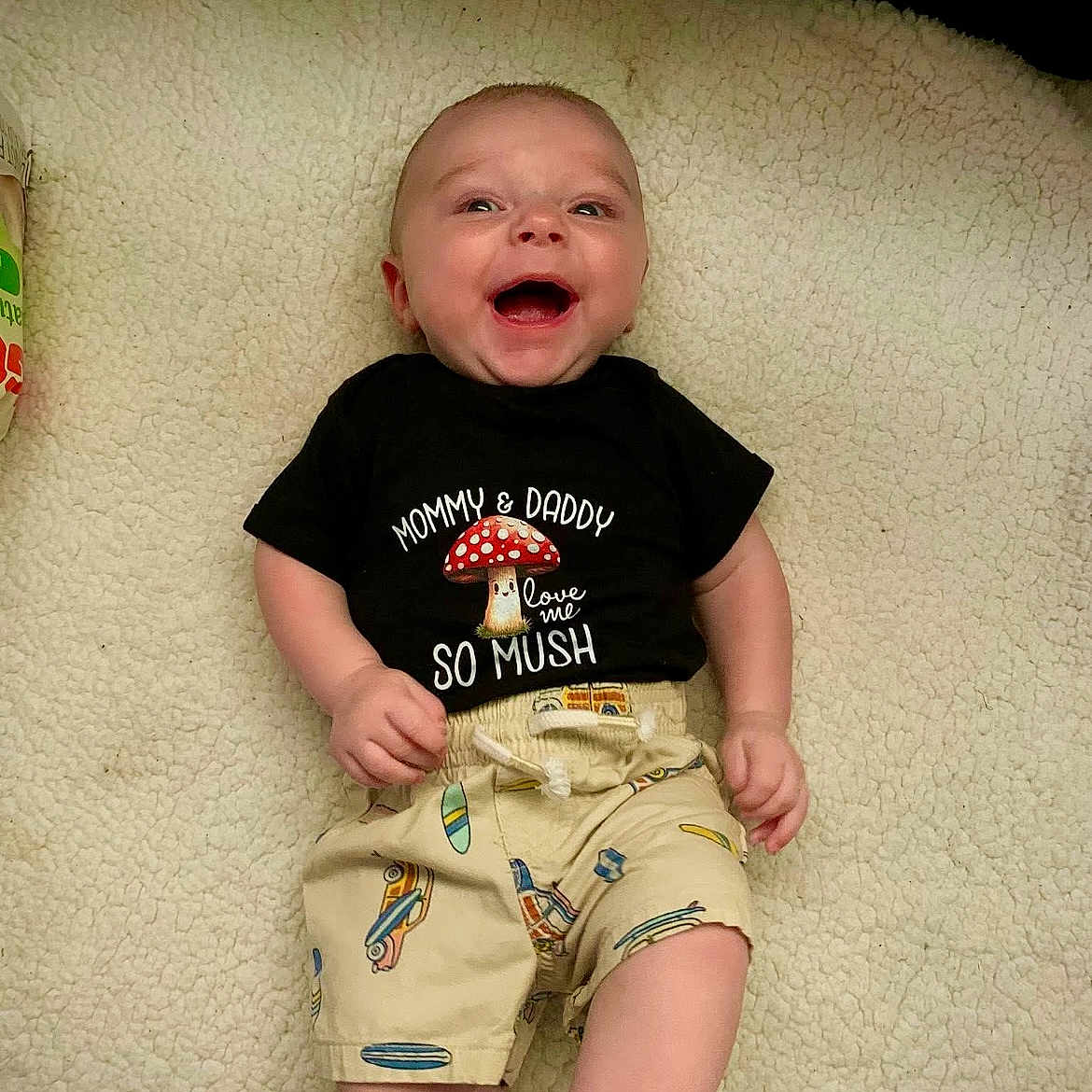A J joined the competition — help win amazing prizes! baby, barefoot, blanket, casual, close_up, clothing, cozy, face, happy, indoor, infant, lying_down, mushroom, onesie, plush_texture, portrait, shirt_text, shorts, skin, smiling