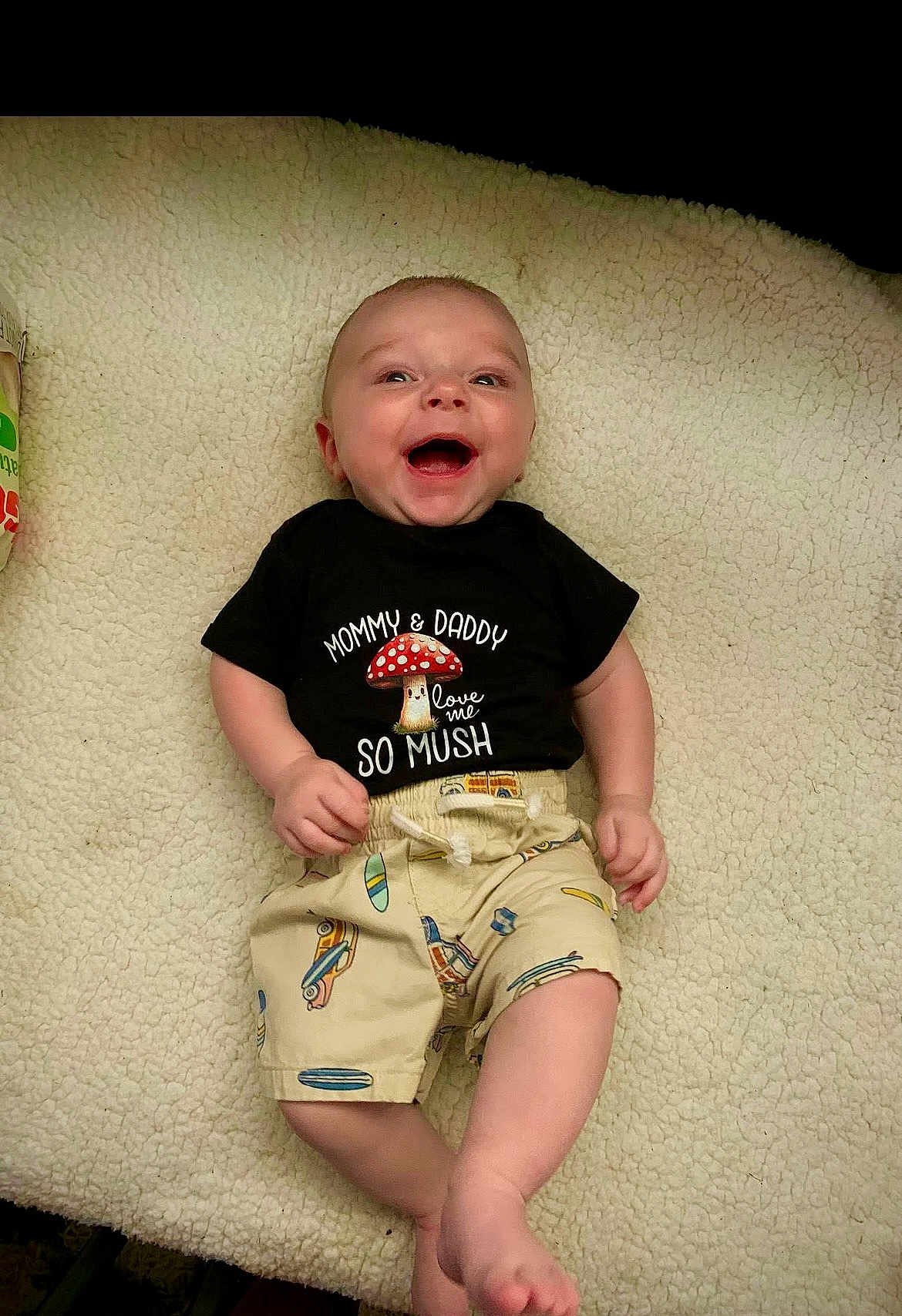 A J joined the competition — help win amazing prizes! baby, barefoot, blanket, casual, close_up, clothing, cozy, face, happy, indoor, infant, lying_down, mushroom, onesie, plush_texture, portrait, shirt_text, shorts, skin, smiling