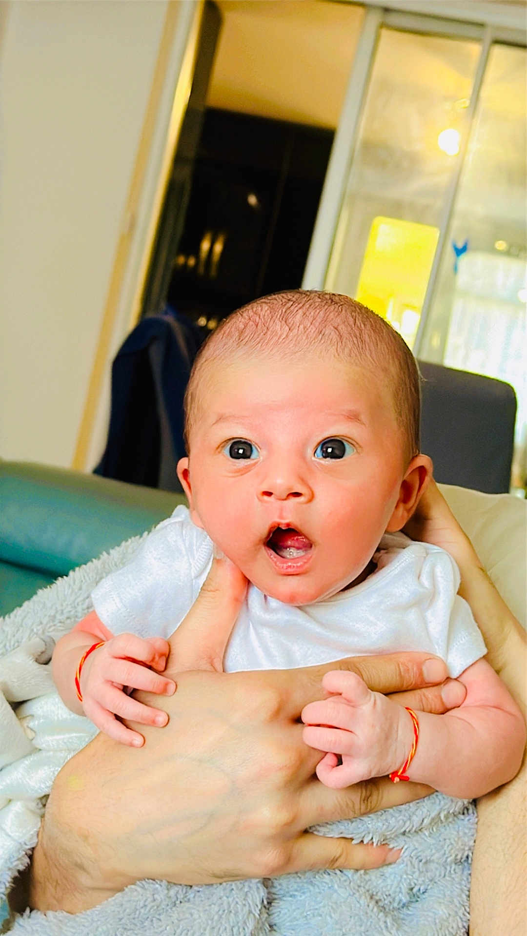Rivani joined the competition — help win amazing prizes! baby, infant, hands, blanket, white_clothing, surprised_expression, indoor, person, skin, face, newborn, holding, cute, young_child, human, portrait, sitting, soft_texture, close_up, bright