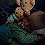 baby, sleeping, pacifier, plush_toy, gingerbread_man, blanket, green_clothing, hand, face, child, soft_toy, cuddle, indoors, cozy, rest, nap, infant, comfort, dark, peaceful