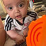 baby, infant, face, eyes, hand, shirt, marvel, toy, orange, carpet, fan, indoor, curious, lying, person, child, closeup, expression, home, floor