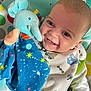 baby, smiling, toy, plush_elephant, blue_blanket, stars_pattern, play_mat, infant, happy, cute, child, clothing, white_shirt, closeup, face, indoor, colorful, comfort, soft_toy, joy