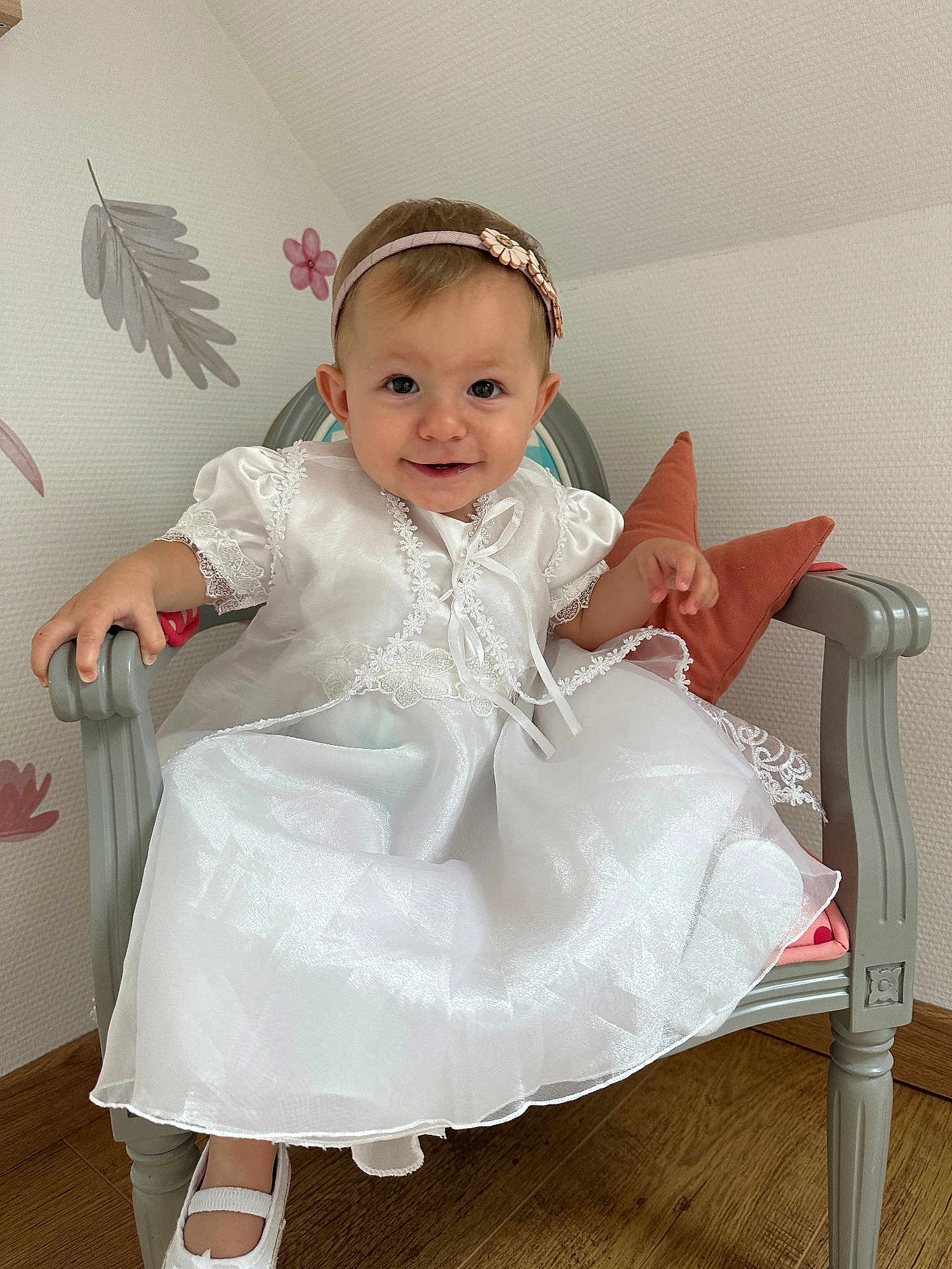 Juliette participe au concours pour gagner de l'argent avec cette photo : baby, child, girl, white_dress, headband, smile, chair, cushion, floor, wooden_floor, wall, flower_decor, leaf_decor, indoors, portrait, cute, sitting, happy, person, footwear